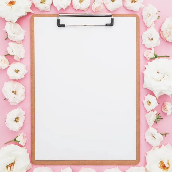 Pembe bir arka plan üzerinde beyaz gül ile çevrili boş kağıdın
