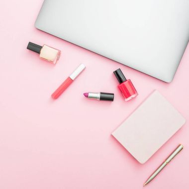 Dizüstü bilgisayar, dizüstü bilgisayar ve pembe bir arka plan üzerinde kozmetik ile ev çalışma masası. Üstten Görünüm. Düz yatıyordu yaşam tarzı kavramı.