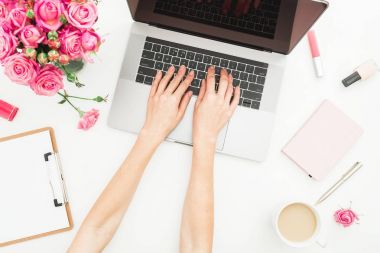 Ev ofis büro. Kadın çalışma alanıyla eller, laptop, pembe gül buketi, aksesuarlar, beyaz üzerine günlüğü. Üstten Görünüm. Düz yatıyordu. Dizüstü bilgisayarda çalışan kız.