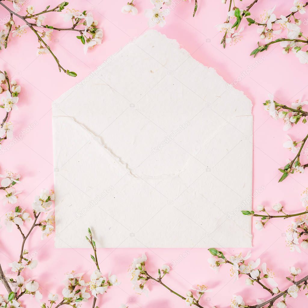 Top view of white envelope surrounded with blooming cherry branches on pink background