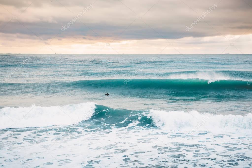 Surfer riding on perfect ocean wave at sunset. Winter surfing in swimsuit  