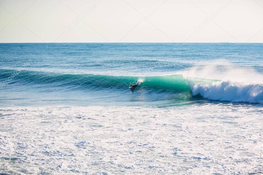 Surfer riding on perfect ocean wave at sunset. Winter surfing in swimsuit  