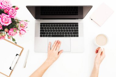 Kadın çalışma alanıyla eller, laptop, pembe gül buketi, kahve kupa beyaz masada