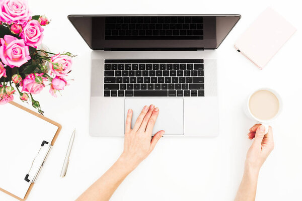 Woman workspace with female hands, laptop, pink roses bouquet, coffee mug on white table