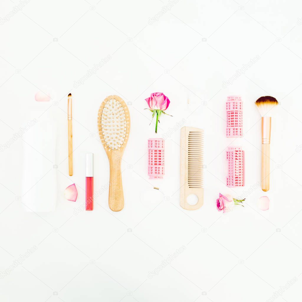 Frame with combs for hair styling, curlers, brushes for make up and pink roses on white background. Beauty blog composition. Flat lay, top view