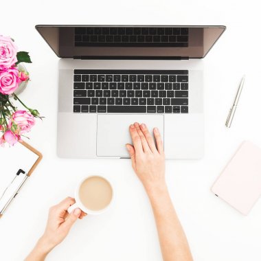 Kadın çalışma alanıyla eller, laptop, pembe gül buketi, kahve kupa beyaz masada