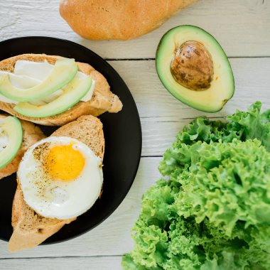 Avokado ve ahşap masa üzerinde siyah plaka üzerinde yumurta sandviç. Lezzetli doğal Kahvaltı