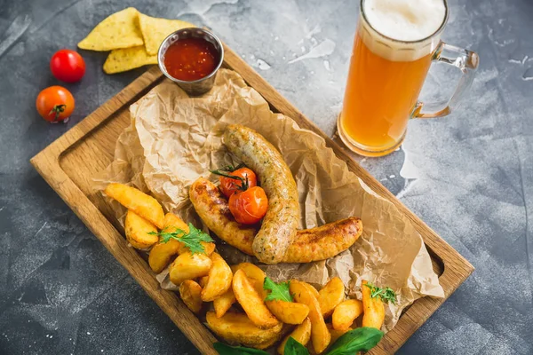 Grilled sausages with fried potatoes and pickled tomato on a wooden plate and glass of beer