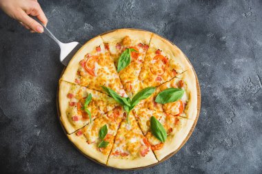 Pastırma, peynir ve domates ve koyu arka plan üzerinde kadınsı el lezzetli pizza. Düz yatıyordu, en iyi görünüm. Gıda arka plan