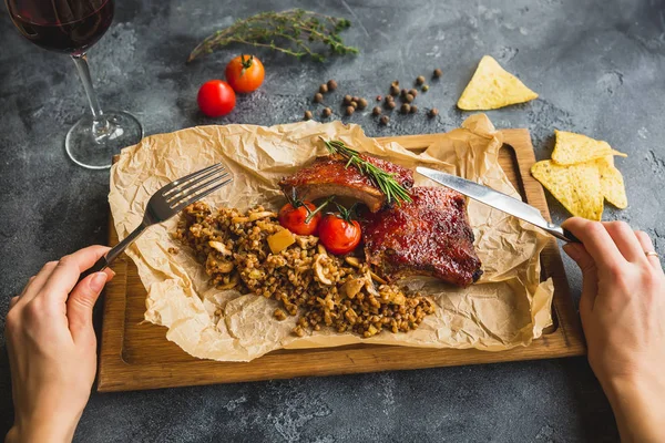 Woman eating darbecued spare ribs, buckwheat with mushroom and tomatoes on old vintage wooden cutting board.