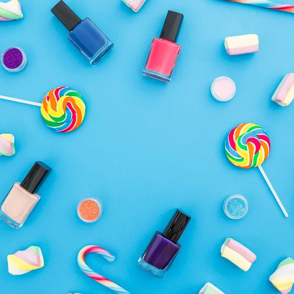 Various cosmetic products with colorful candies on blue background