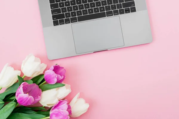 Laptop and tulips flowers on pink background. Flat lay. Top view. Composition with copy space.