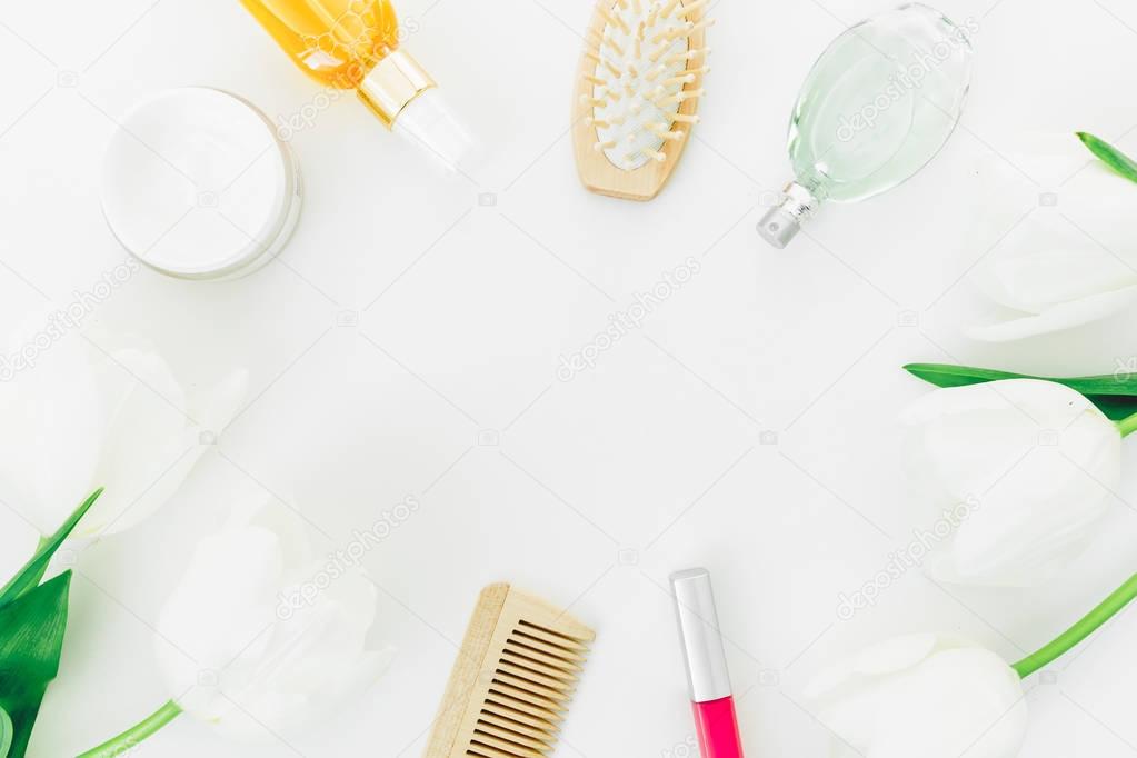 Frame with perfume, cosmetics, combs and tulips flowers on white background. Beauty blogger composition. Flat lay, top view