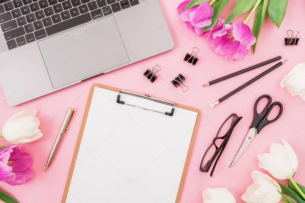 Laptop, clipboard, tulips flowers, glasses and accessories on pink background. Flat lay. Top view. Freelancer office concept