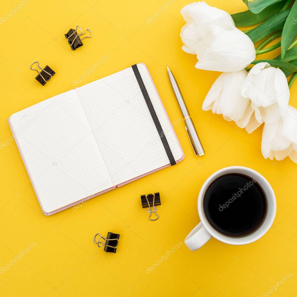 Top view of blanket notebook with cup of coffee and white tulips on yellow background