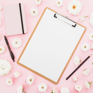 Pano, defter ve kalem ile pembe bir arka plan üzerinde beyaz gül. Düz yatıyordu, en iyi görünüm. İş kavramı.