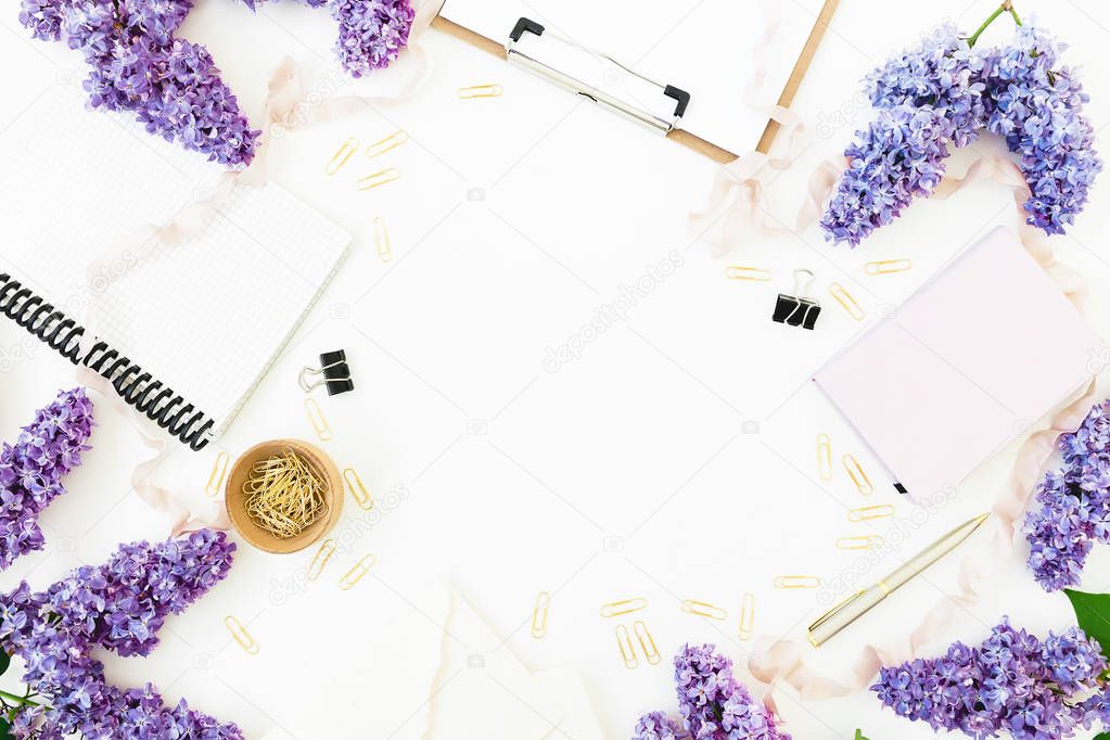 Blogger workspace with clipboard, dairy, envelope, lilac flowers and accessories on white background. Flat lay, top view.