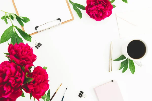 Blogger or freelancer workspace with clipboard, dairy, peony flowers and coffee mug on white background. Flat lay, top view. Beauty blog concept with copy space