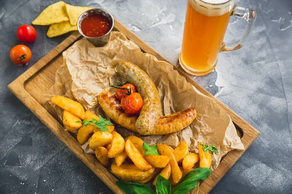 Fried sausages with fried potatoes and pickled tomato on wooden plate and glass of beer