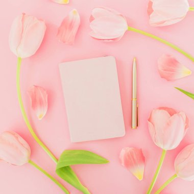 Defter ve kalem ile güzel Lale çiçek üstten görünüm pastel pembe bir arka plan üzerinde