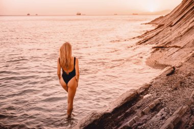 siyah Yüzme elbiseli güzel sarışın kadının fotoğrafını görünümü'nde Günbatımı kumsalda geri