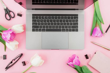 Laptop, günlük, çiçekler, bardaklar, kalem ve makas pembe üzerine. Düz 