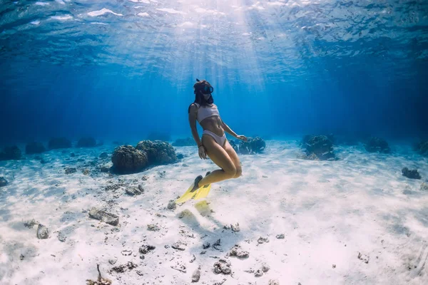 Free diver young girl with yellow fins glides over sandy bottom — Stock Photo, Image