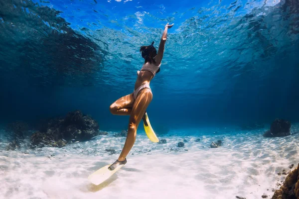 Volný potápěč mladá dívka se žlutými ploutve klouže přes písčité dno — Stock fotografie