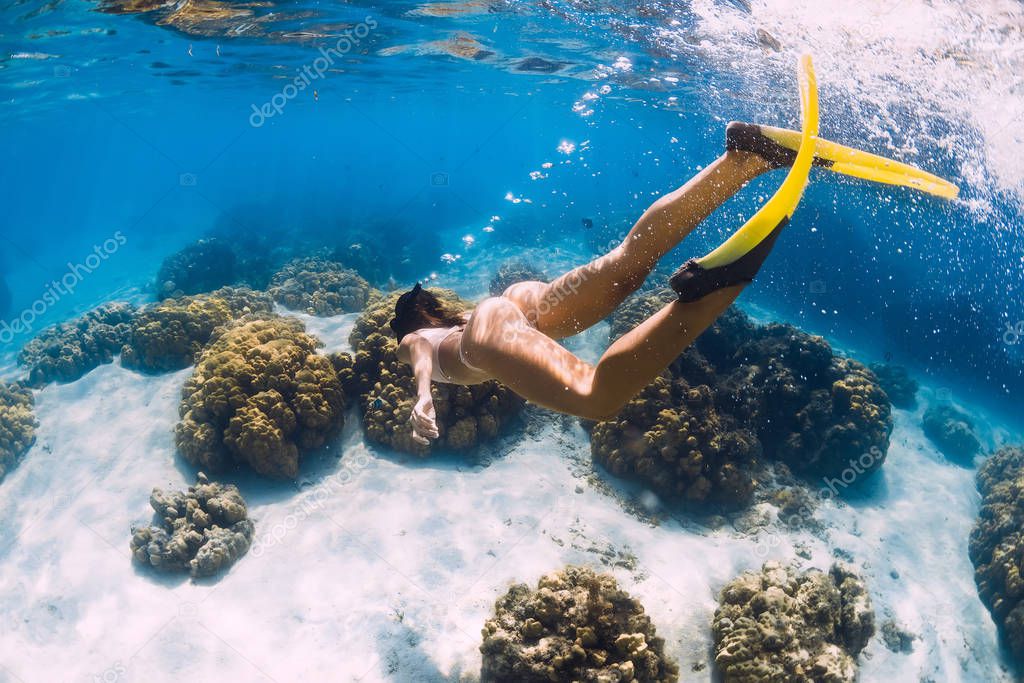 Free diver young girl with yellow fins glides over sandy bottom 