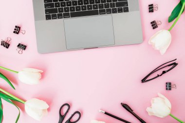 Laptop, çiçekler, bardaklar, pembe arka planda kalem ve makas. F