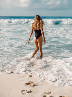 Bikinili çekici genç kadın tropikal plajda ve okyanusta rahatlıyor.