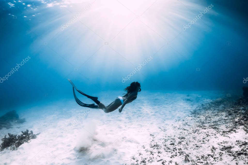 Free diver girl with fins glides over sandy sea in ocean. Freedi
