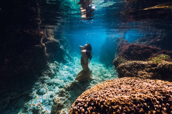 Frau im Bikini posiert unter Wasser nahe Korallen im Ozean. — Stockfoto