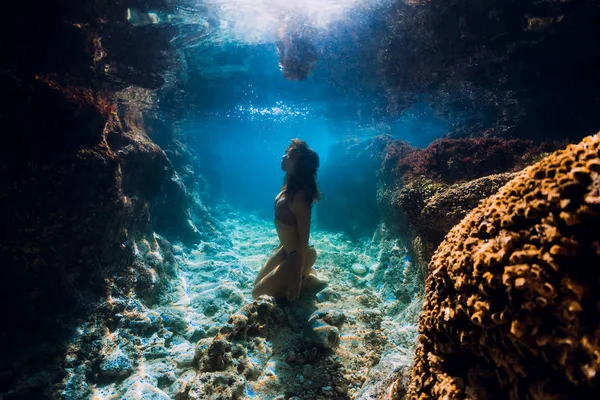 Žena v bikinách pózuje pod vodou v blízkosti korálů v oceánu. — Stock fotografie