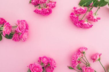 Pembe arka planda gül çiçeklerinden yapılmış çiçek çerçevesi. Düz yatıyordu,