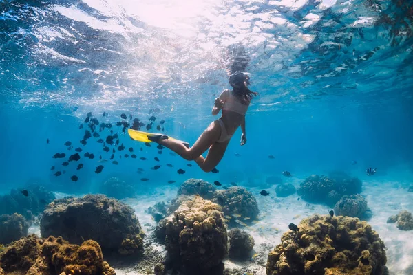 Vrouw glijdt onder water met gele vinnen over zandige zee en cora — Stockfoto