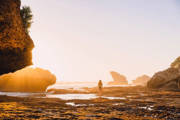 Reiziger vrouw in badpak poseren bij zonsondergang in de buurt van oceaan en rots — Stockfoto