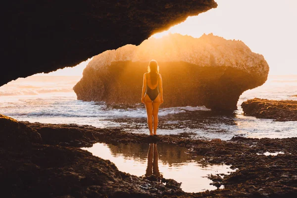 Femme voyageuse en maillot de bain posant au coucher du soleil près de l'océan et de la roche — Photo