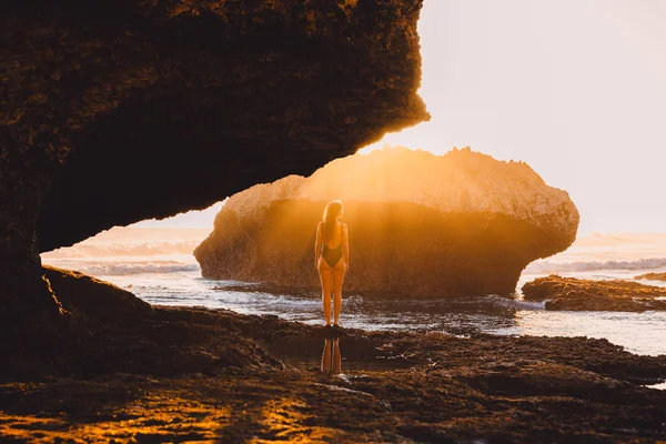 Женщина-путешественница в купальнике позирует на закате у океана и скалы — стоковое фото