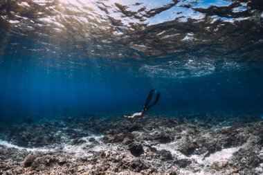 Yüzgeçli bir kadın, mavi okyanusta suyun altında süzülüyor. Okyanusta serbest dalış ya da yüzme