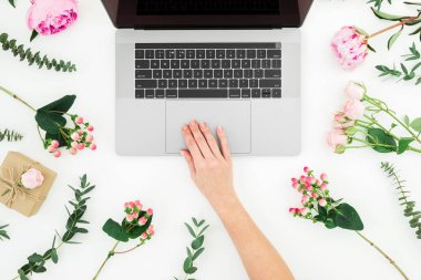 Kadın dizüstü bilgisayarda çalışıyor. Dizüstü bilgisayarı ve beyaz arka planda pembe çiçekleri olan kadın elleri. Üst Manzara. Düz yatıyordu.