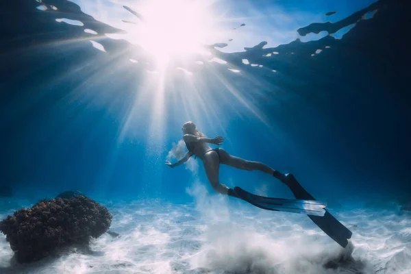 Woman free diver glides with white sand over sandy sea. Freediving underwater in Hawaii island