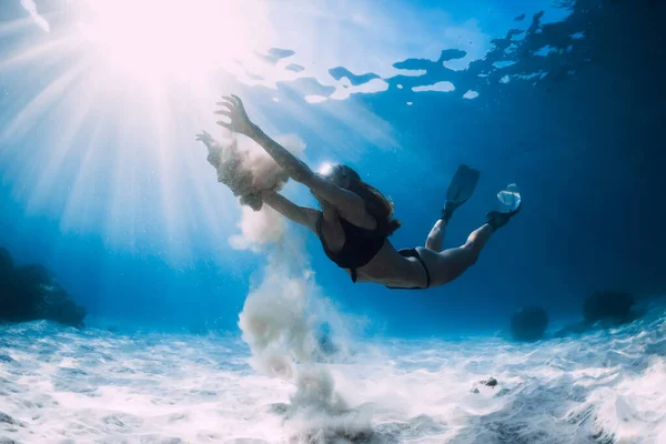 Woman free diver glides with white sand over sandy sea. Freediving underwater in Hawaii island