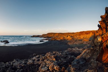 Lanzarote, Kanarya Adaları 'nda gün batımında lav kayalıkları ve okyanus olan bir sahil..