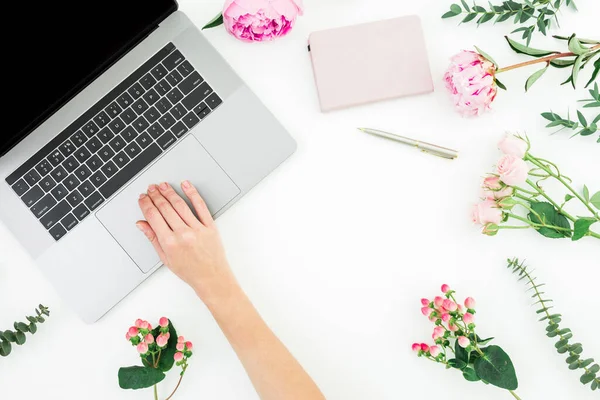 Woman working with laptop. Female hands with laptop and pink flowers on white background. Top view. Flat lay.