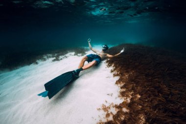 Serbest dalış yüzgeçli adam mavi okyanusta kumlu zeminde rahatlar.