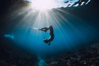 Yüzgeçli serbest dalgıç kadın mercan zeminde süzülüyor ve inanılmaz güneş ışınları var. Okyanusta serbest dalış