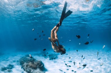 Yüzgeçli serbest dalgıç kız mavi okyanusta tropik balıklarla kumlu zeminde süzülüyor.