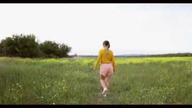 Sarı çiçeklere dokunarak bir tarlada yürümekten mutlu genç bir kadın. Güzel kaygısız kadın çiçek açan tarlada doğanın tadını çıkarıyor.