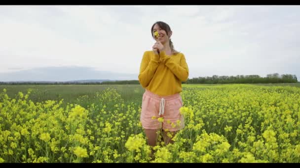 年轻的女人高兴地穿过田野 触摸着黄色的花朵 美丽无忧无虑的女人在繁茂的田野里享受大自然 — 图库视频影像